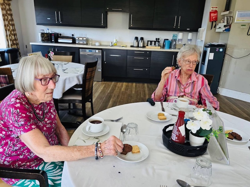 2 of our residents sat at the table with a hot drink and biscuits together