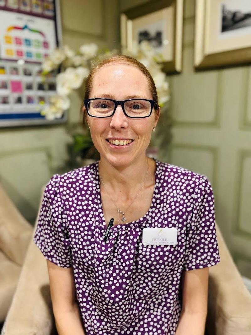 Lady with glasses on, smiling and wearing a purple and white spotty top having a headshot taken for the Harrier Grange team page