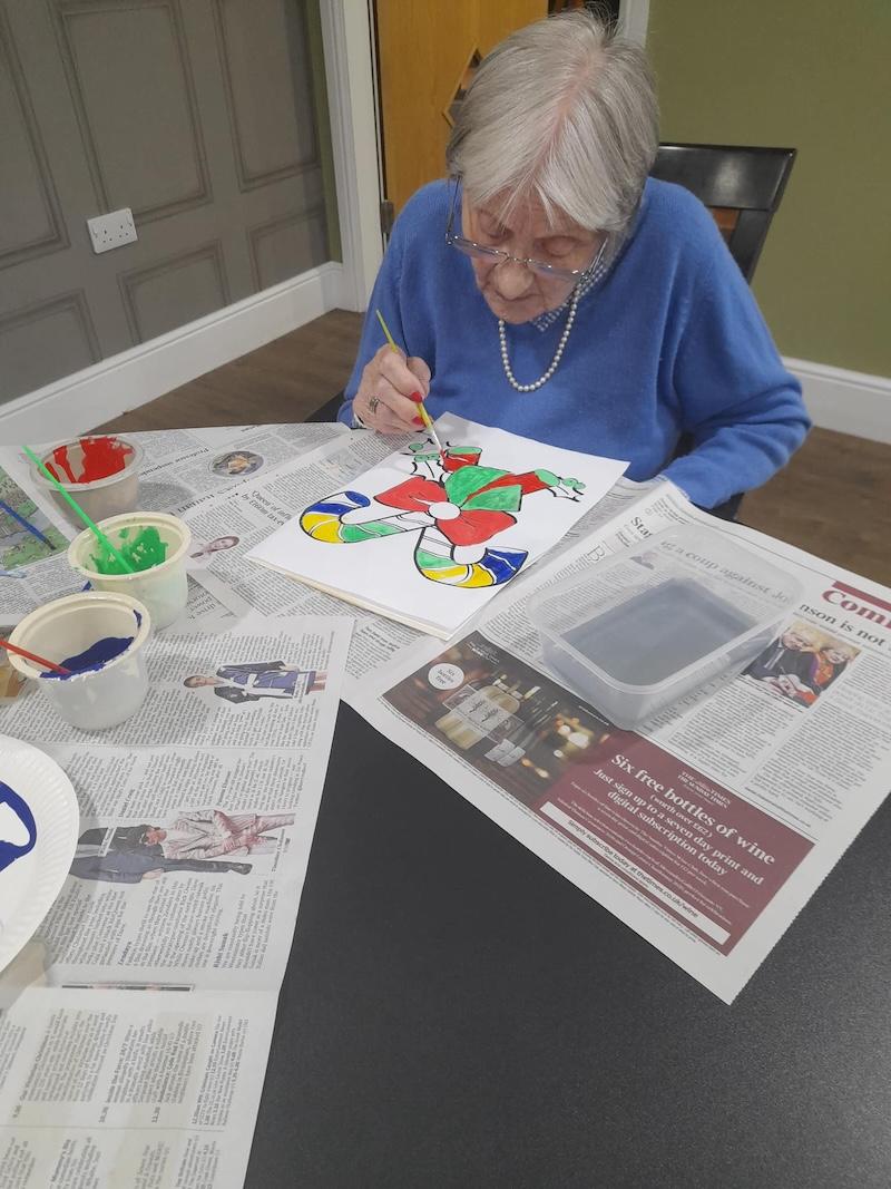elderly lady sat down painting candy canes