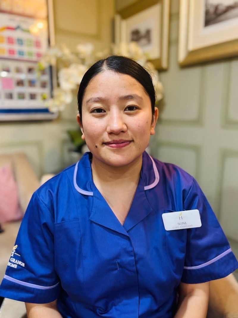 Woman with brown hair sat in an armchair wearing a purple care assistant uniform