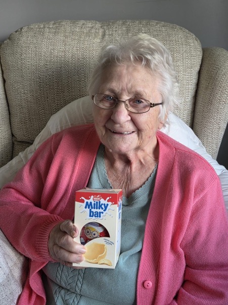 older lady wearing glasses holding a milky bar easter egg