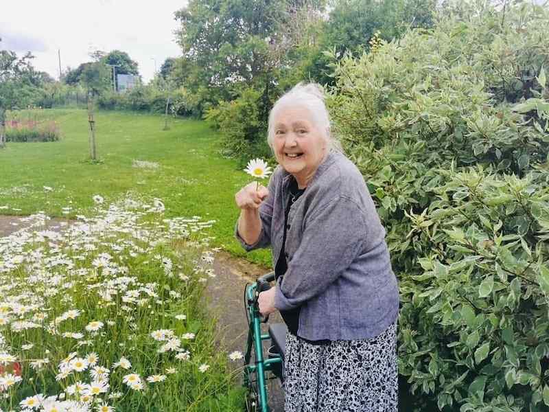 resident holding a white flower in the local park smiling