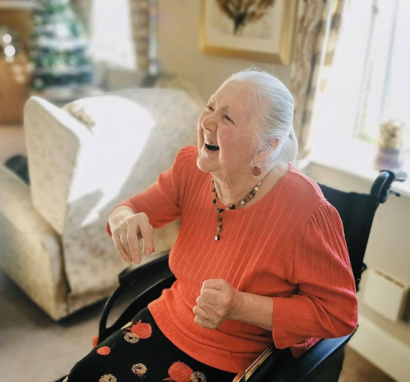 female resident sat in her wheelchair in the lounge smiling