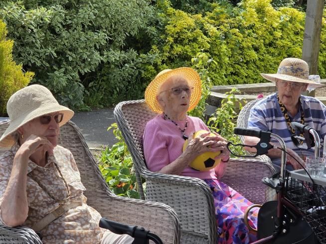 older adults sat outside in a garden and a lady holding a yellow ball