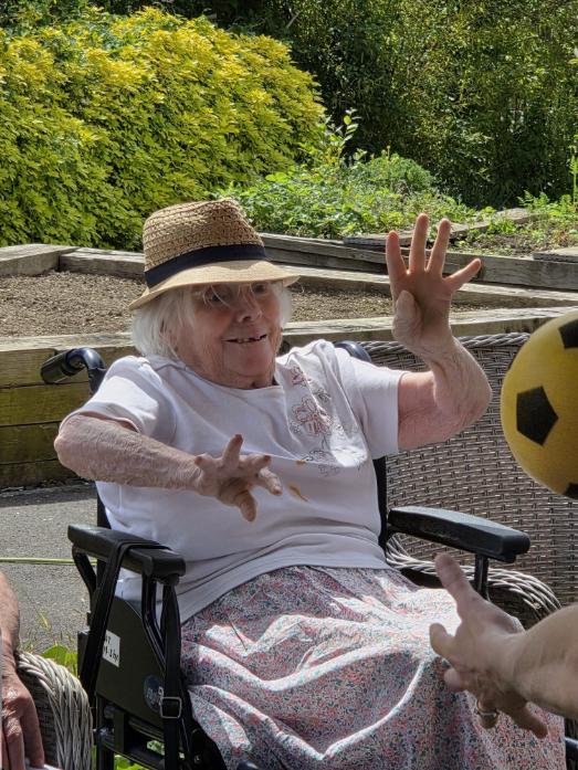 older lady sat in a wheelchair throwing a yellow ball
