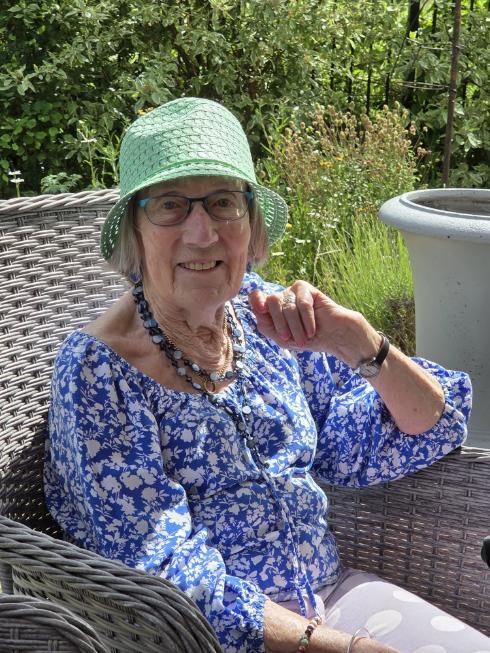 older lady wearing a green bucket hat sat in a chair in a garden