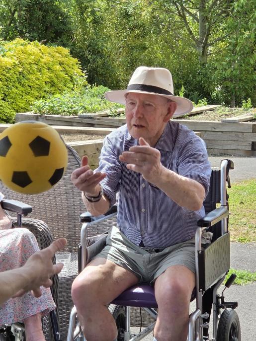 older man sat in a wheelchair throwing a yellow ball